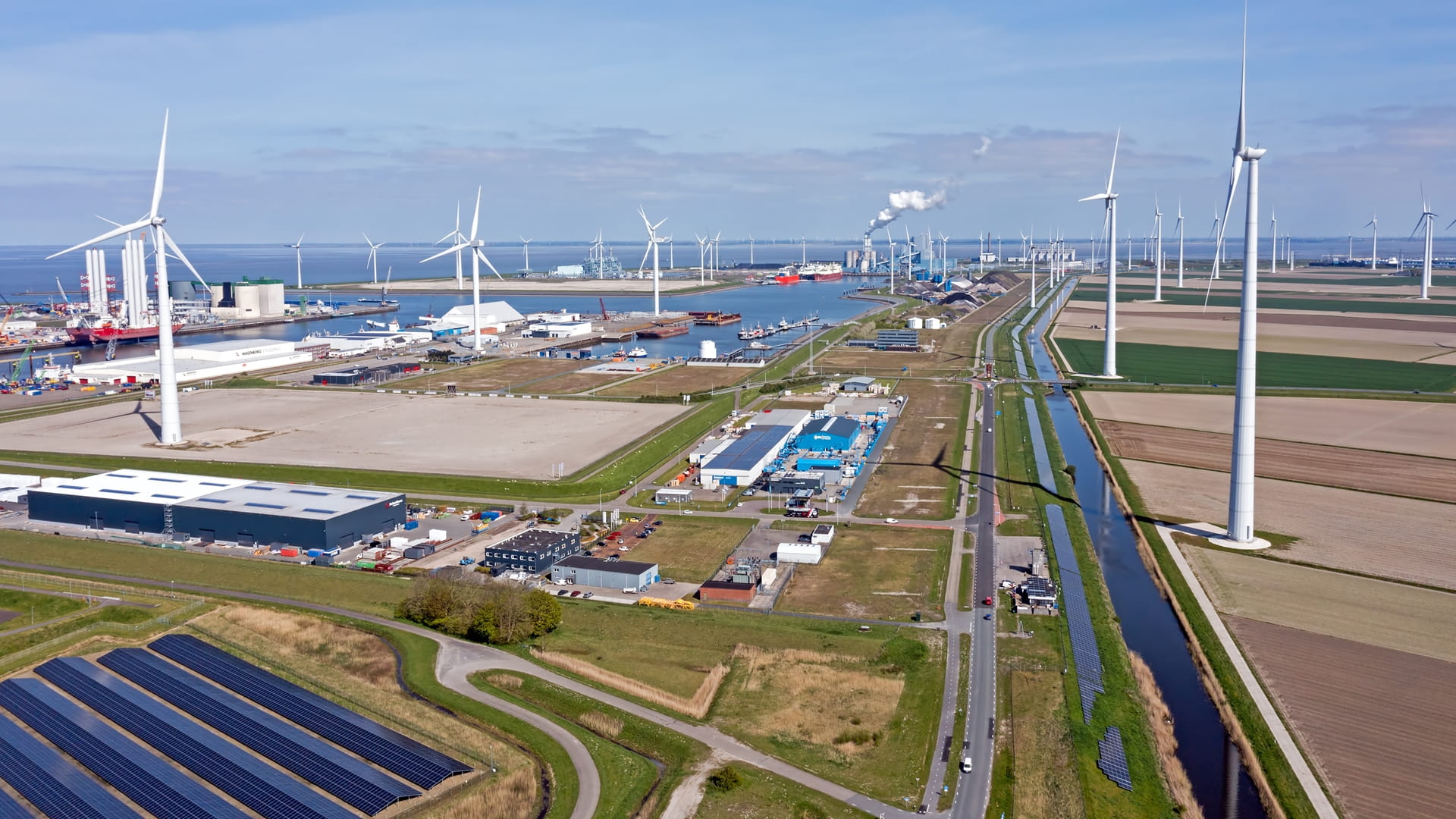 An aerial view of a harbor with wind turbines and solar panels. This is an example of maritime decarbonization. Wind and solar power are two renewable energy sources that can help to decarbonize the maritime industry.